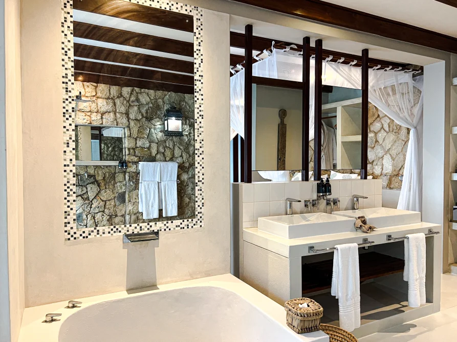 Boutique hotel bathroom with a bathtub, double sinks, large mirrors, and a stone feature wall.