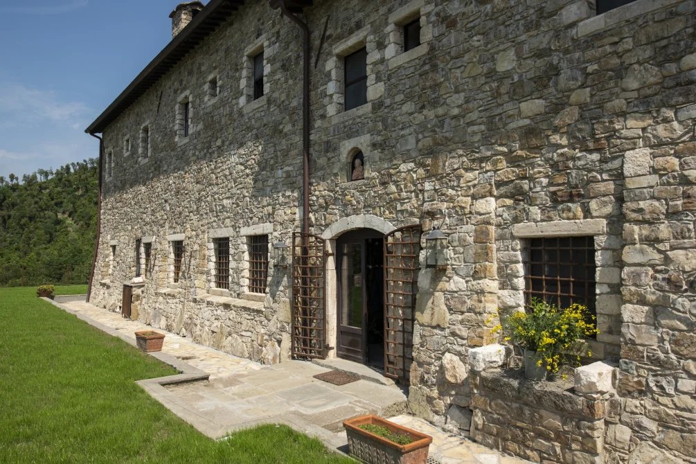 Stone exterior of Eremito Hotelito with arched entrance, iron window grilles, and a sunlit terrace beside a green lawn.