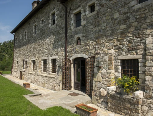 Stone exterior of Eremito Hotelito with arched entrance, iron window grilles, and a sunlit terrace beside a green lawn.
