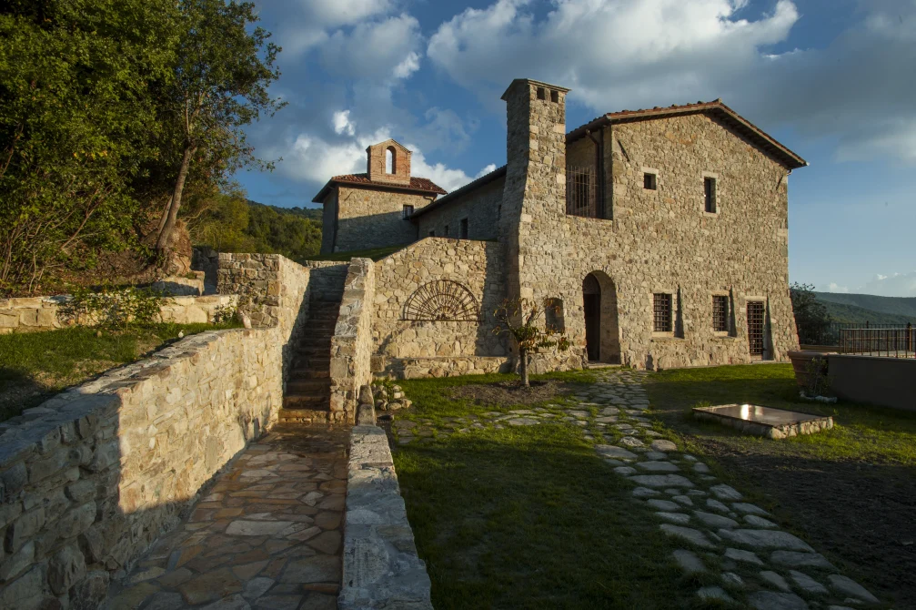 Stone buildings of Eremito Hotelito in warm afternoon light with a terrace path, steps, and hillside views under a partly cloudy sky.