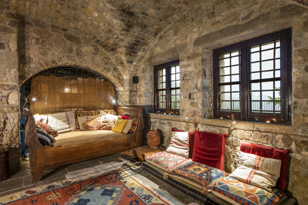 Stone-vaulted bedroom lounge at Eremito Hotelito with a wooden daybed, colorful cushions, and large windows overlooking the hills.