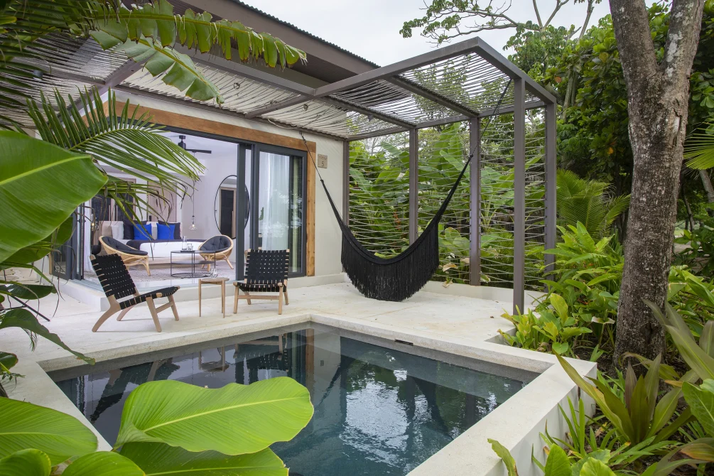 Private bungalow patio with a plunge pool, lounge chairs, and a hammock under a shaded pergola surrounded by tropical plants.